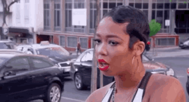 a woman with short hair and red lipstick is standing on a street with cars .