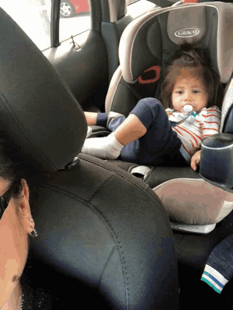 a baby is sitting in a graco car seat with a pacifier in her mouth