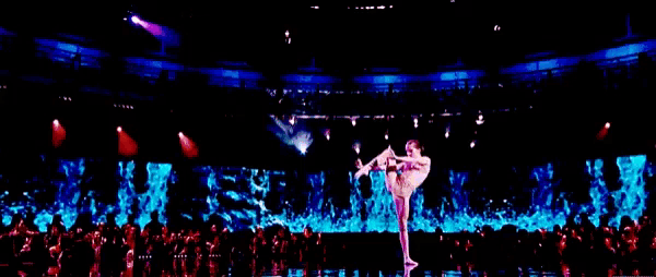 a woman is dancing on a stage in front of a crowd of people in a stadium .