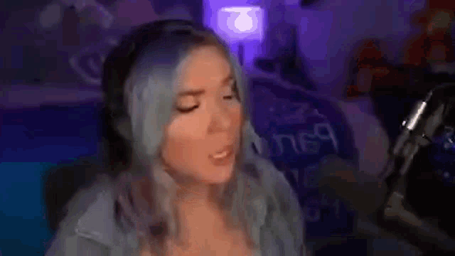 a woman with blue hair is sitting in front of a microphone in a room .