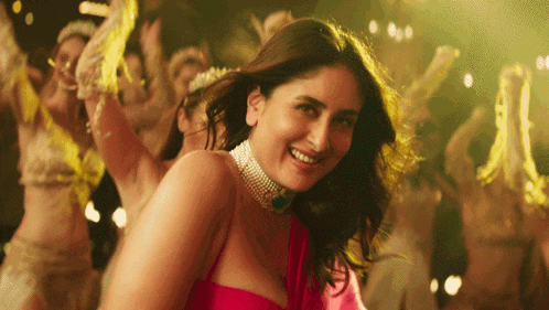 a woman in a pink dress is smiling in front of a group of dancers