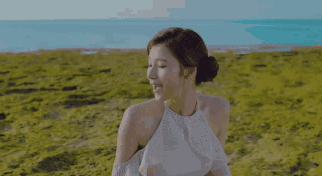 a woman in a white dress is sitting in a field near the ocean