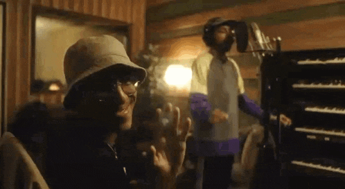 a man wearing a bucket hat and sunglasses is standing in front of a microphone in a recording studio .