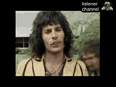 a close up of a man with long hair wearing a yellow jacket and a necklace .