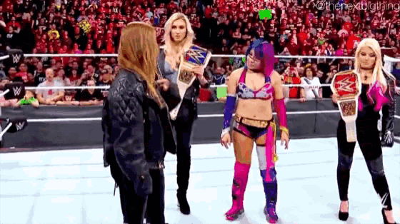 a group of female wrestlers are standing on a wrestling ring holding championship belts .