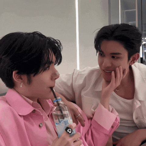 a man in a pink shirt is drinking from a bottle with a straw that says ' aquafina ' on it