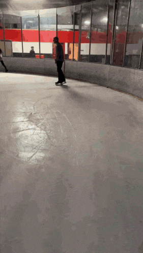 a person is ice skating on a rink with a red and white wall