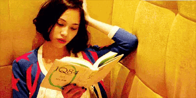 a woman is reading a book called q8 while leaning against a wall .