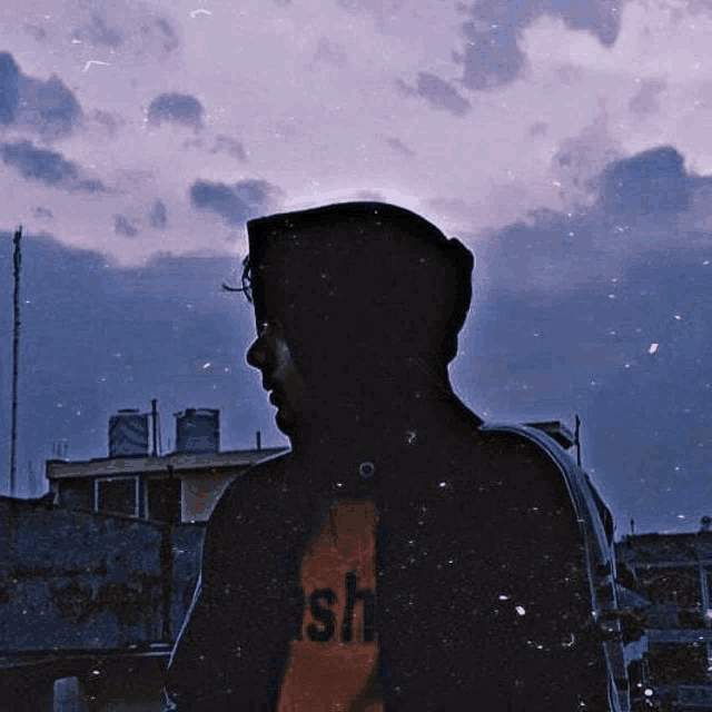 a man in a hoodie is standing in front of a cloudy sky at night .