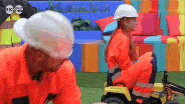 a man and a woman wearing hard hats and orange overalls are playing with a toy tractor that says big brother