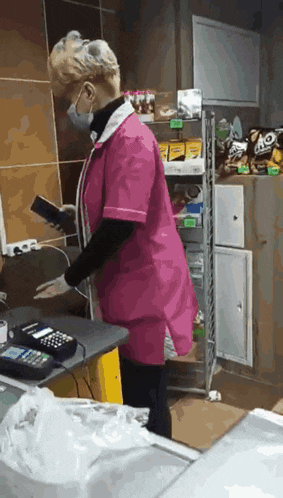 a woman wearing a mask and a pink apron is using a calculator