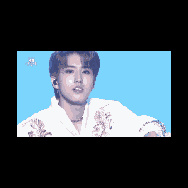 a young man wearing a white shirt and gold embroidery is on a stage