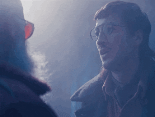 a man with glasses and a beard looks at another man