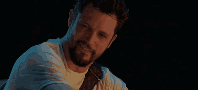 a man with a beard is smiling and playing a guitar in a dark room .