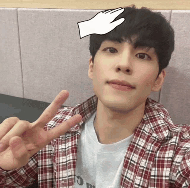 a young man wearing a plaid shirt is making a peace sign with his hands