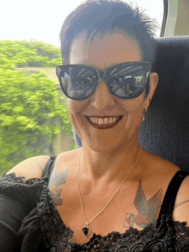 a woman wearing sunglasses and a black lace top smiles