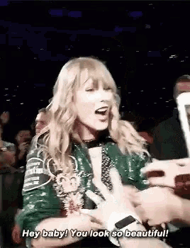 a woman in a green jacket is talking to a fan in a crowd and says `` hey baby ! you look so beautiful ! ''
