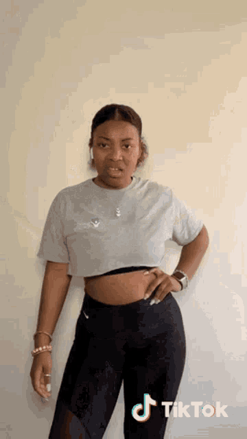 a woman wearing a grey crop top and black leggings is standing in front of a wall .