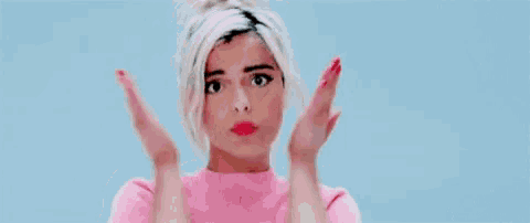 a woman in a pink shirt is holding her face with her hands and making a funny face .