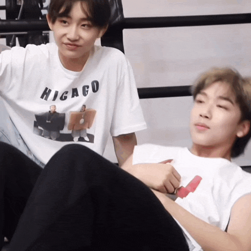 a man wearing a higago t-shirt sits next to another man in a boxing ring