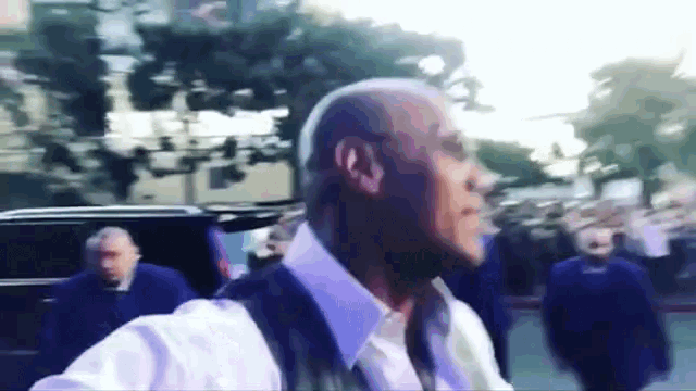 a bald man in a white shirt and vest walks down a street