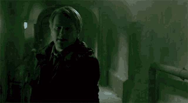 a man is standing in a dark room with a green light behind him and looking at the camera .