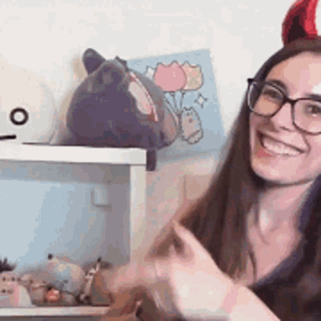 a woman wearing glasses and a red and white hat is smiling in front of a shelf with stuffed animals .