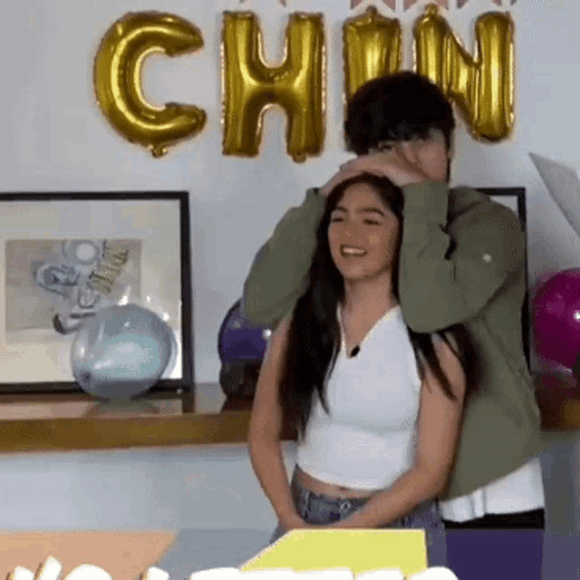 a man is putting his hand on a woman 's head in front of a wall with the word chin balloons .