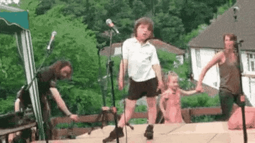 a group of people are dancing on a stage in front of a microphone while holding hands .