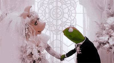 miss piggy and kermit the frog are getting married in a wedding dress and holding hands .