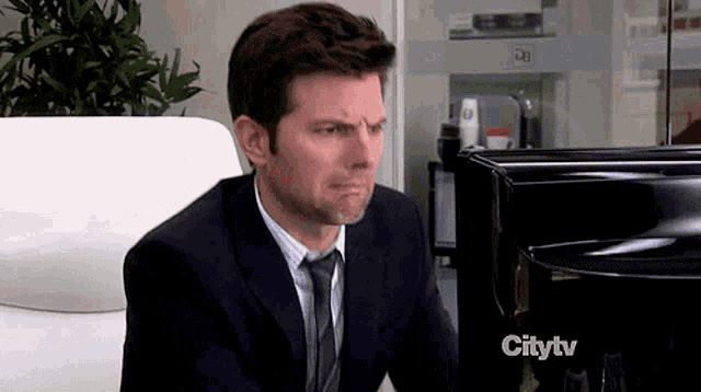 a man in a suit and tie is sitting in front of a citytv monitor
