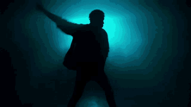 a silhouette of a man dancing in a dark room with a light behind him .