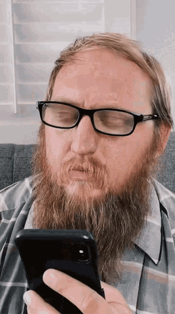 a man with a beard wearing glasses is looking at his phone