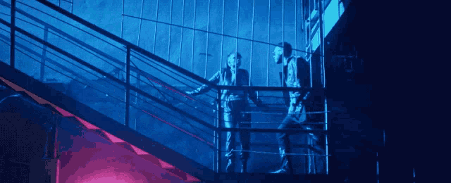 two men are walking up a set of stairs in a dark room with a sign that says ' emergency exit ' on it