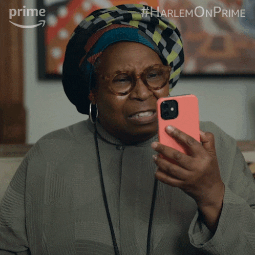 a woman wearing glasses and a turban is looking at her phone with the hashtag #harlemonprime at the bottom