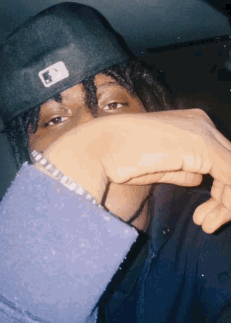 a man covering his face with his hand and wearing a hat