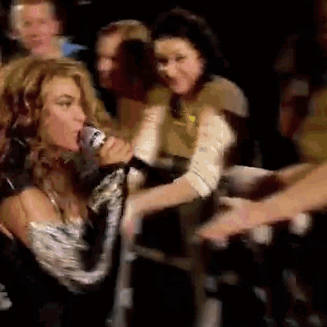 a woman is singing into a microphone in front of a crowd