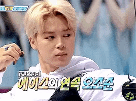 a young man with blonde hair is holding a remote control in his hand and looking at the camera .