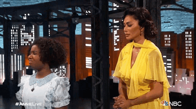 a woman in a yellow dress stands next to another woman in a white dress on nbc annie live