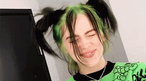 billie eilish is wearing a green shirt and has green hair .