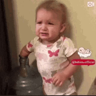 a baby is crying while standing next to a water cooler .