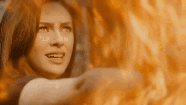a woman is standing in front of a wall of fire .