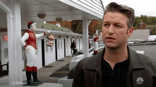 a man wearing a nbc jacket stands in front of a building