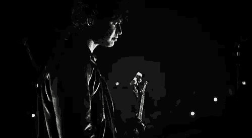 a black and white photo of a young man in a leather jacket playing a guitar on stage .