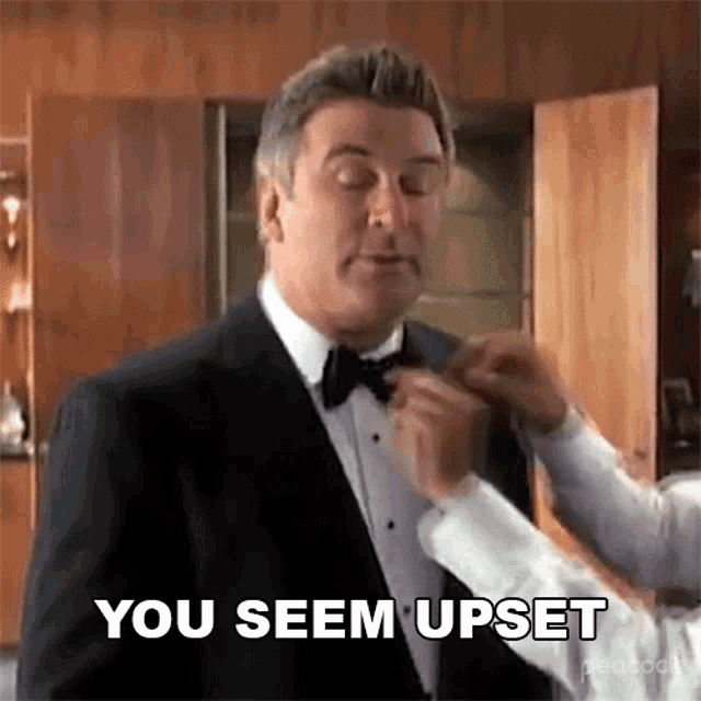 a man in a tuxedo is getting his bow tie adjusted by a man in a white shirt .