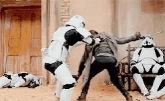 a group of stormtroopers are fighting each other in a sandy field .