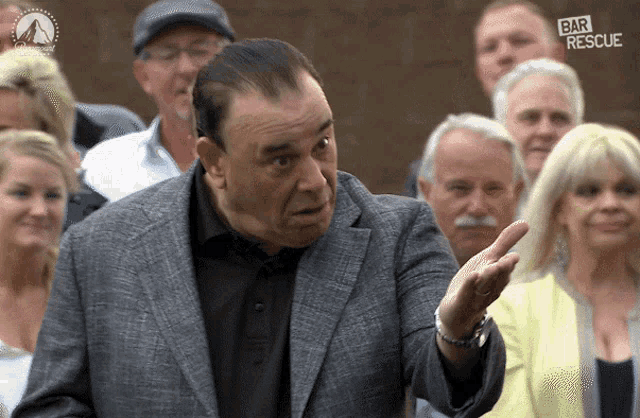 a man in a suit stands in front of a group of people with bar rescue written on the bottom