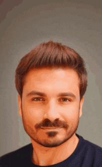 a man with a beard wearing a blue shirt is smiling for the camera