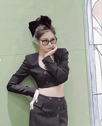 a woman wearing glasses and a bow in her hair stands in front of a window