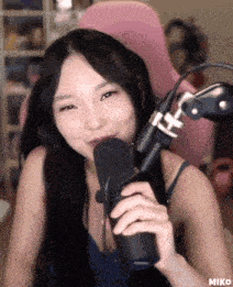 a woman is holding a microphone in front of a pink chair with the word miko on the bottom